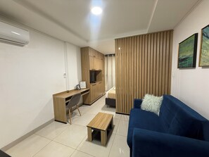 Ein kompakter Wohnraum mit Küchenzeile, einem blauen Sofa, einem kleinen Holztisch und einer Trennwand mit vertikalen Lamellen.