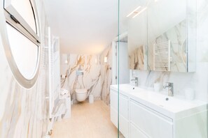 Ein modernes Badezimmer mit Marmorwänden, einer Duschkabine aus Glas und einem weißen Waschtisch mit großem Spiegel.