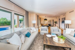 Een moderne woonkamer met een bank, fauteuils, een salontafel en een eethoek op de achtergrond.