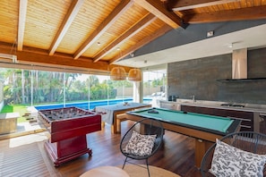 Een moderne keuken met een pooltafel, tafelvoetbal en een eethoek met uitzicht op een zwembad.