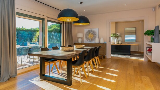 Un comedor moderno con una mesa de madera, sillas negras e iluminación colgante.