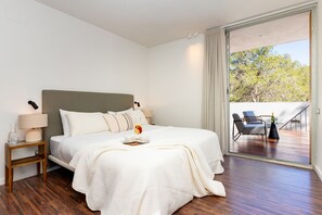 Ein Hotelzimmer mit Bett, Nachttisch, Lampe und Blick auf eine Terrasse.