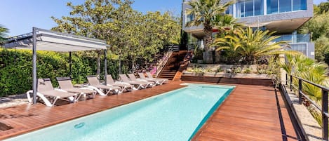A swimming pool with lounge chairs, a wooden deck, and a modern building with large windows.