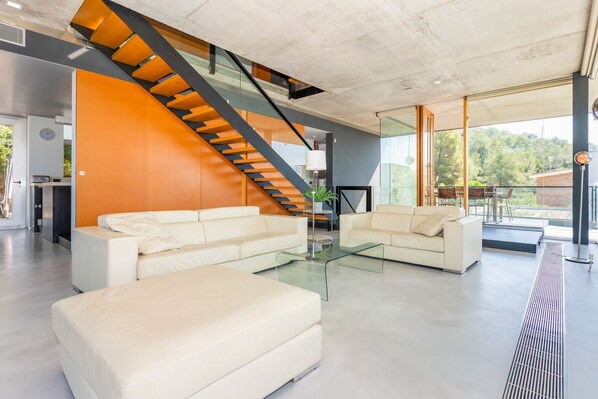 Un salon moderne avec un escalier, deux canapés, une table basse et une vue sur l’extérieur.