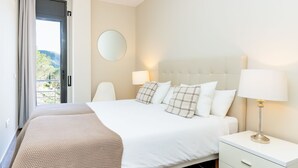 Habitación de hotel con cama, lámparas de noche, un espejo redondo y vistas a través de una puerta abierta.