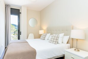 Ein Hotelzimmer mit Bett, Nachttischlampen, einem runden Spiegel und Blick durch eine offene Tür.
