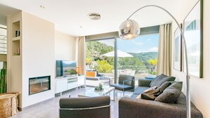 Un salón moderno con televisión de pantalla plana, un sofá, una mesa de centro y un balcón con mobiliario de exterior.