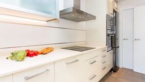 Una cocina moderna con armarios blancos, una campana extractora de acero inoxidable, un horno empotrado y una encimera con verduras y pan.