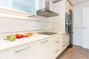 Eine moderne Küche mit weißen Schränken, einer Edelstahl-Dunstabzugshaube, einem Einbauofen und einer Arbeitsplatte mit Gemüse und Brot.