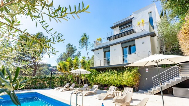 Una casa moderna de dos pisos con piscina, mobiliario exterior y una escalera que conduce al nivel superior.