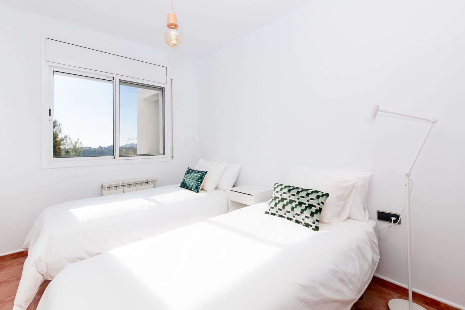 Een slaapkamer met twee bedden, een raam, een nachtkastje en een vloerlamp.