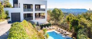 A modern multi-story building with balconies, a swimming pool, and a view of the surrounding landscape.