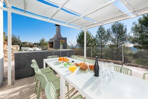 Ein Essbereich im Freien mit einem für das Frühstück gedeckten Tisch, einem Grill und Blick auf die umliegende Landschaft.