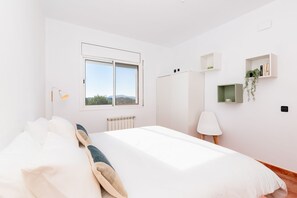 Ein Schlafzimmer mit Bett, Fenster, Heizkörper, Schreibtisch und Regalen mit Pflanzen.