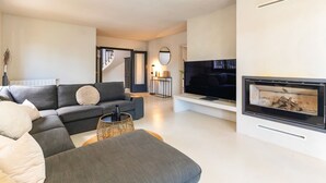 A modern living room with a sofa, television, fireplace, and a staircase leading to another level. - Villa Caliza I - Four Bedroom Villa, Sleeps 8 (Cunit)