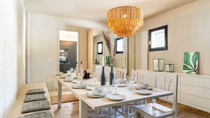 A dining area with a long table set for four, a chandelier, and a view into the kitchen. - Villa Caliza I - Four Bedroom Villa, Sleeps 8 (Cunit)
