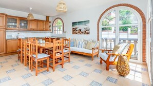 Una cocina amplia con armarios de madera, una mesa de comedor y sillas. Hay un ventanal con vistas a zonas verdes.