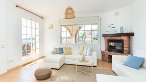 Una sala de estar con un sofá blanco, una mesa de centro, una chimenea y un ventanal grande.