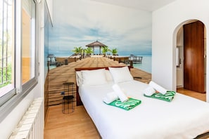 A bedroom with a bed, a view of a wooden deck leading to a beach, and a door to another room. - Villa Charma - Three Bedroom Villa, Sleeps 9 (Vora-sitges)