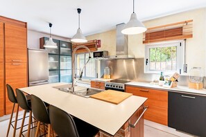 A modern kitchen with a central island, stainless steel appliances, and wooden cabinetry. - Villa Charma - Three Bedroom Villa, Sleeps 9 (Vora-sitges)