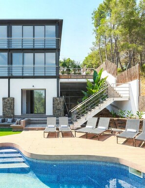 Ein modernes, zweistöckiges Haus mit Swimmingpool, Außenbereich mit Sitzgelegenheiten und einer Treppe, die zum Obergeschoss führt.