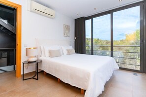 Ein Schlafzimmer mit einem großen Bett, einem Nachttisch mit Lampe, einem Fenster mit Aussicht und einer Klimaanlage.
