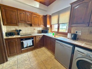A kitchen with wooden cabinets, a microwave, a dishwasher, and a washing machine. - Serenity Villa - Private Heated Swimming Pool (Liopetri)