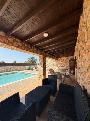 Un espacio al aire libre cubierto con piscina, paredes de piedra y mobiliario exterior.