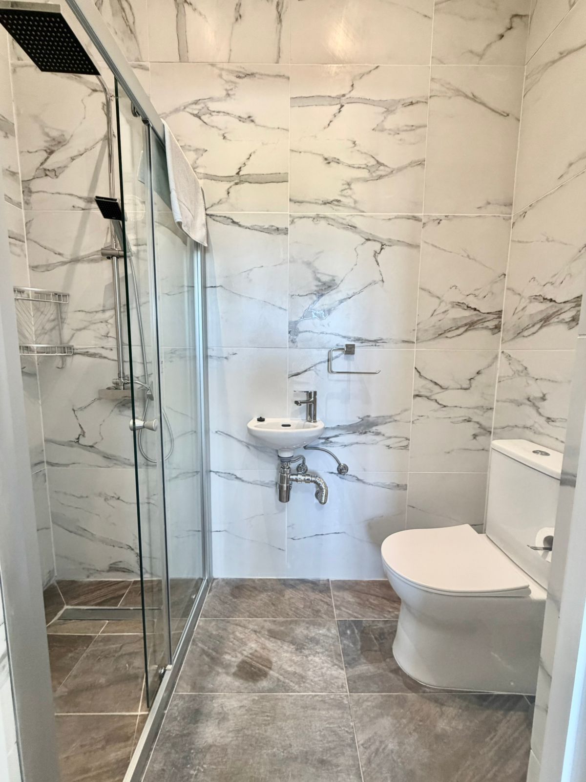 Ein Badezimmer mit einer Duschkabine, einem weißen Waschbecken und einer Toilette.