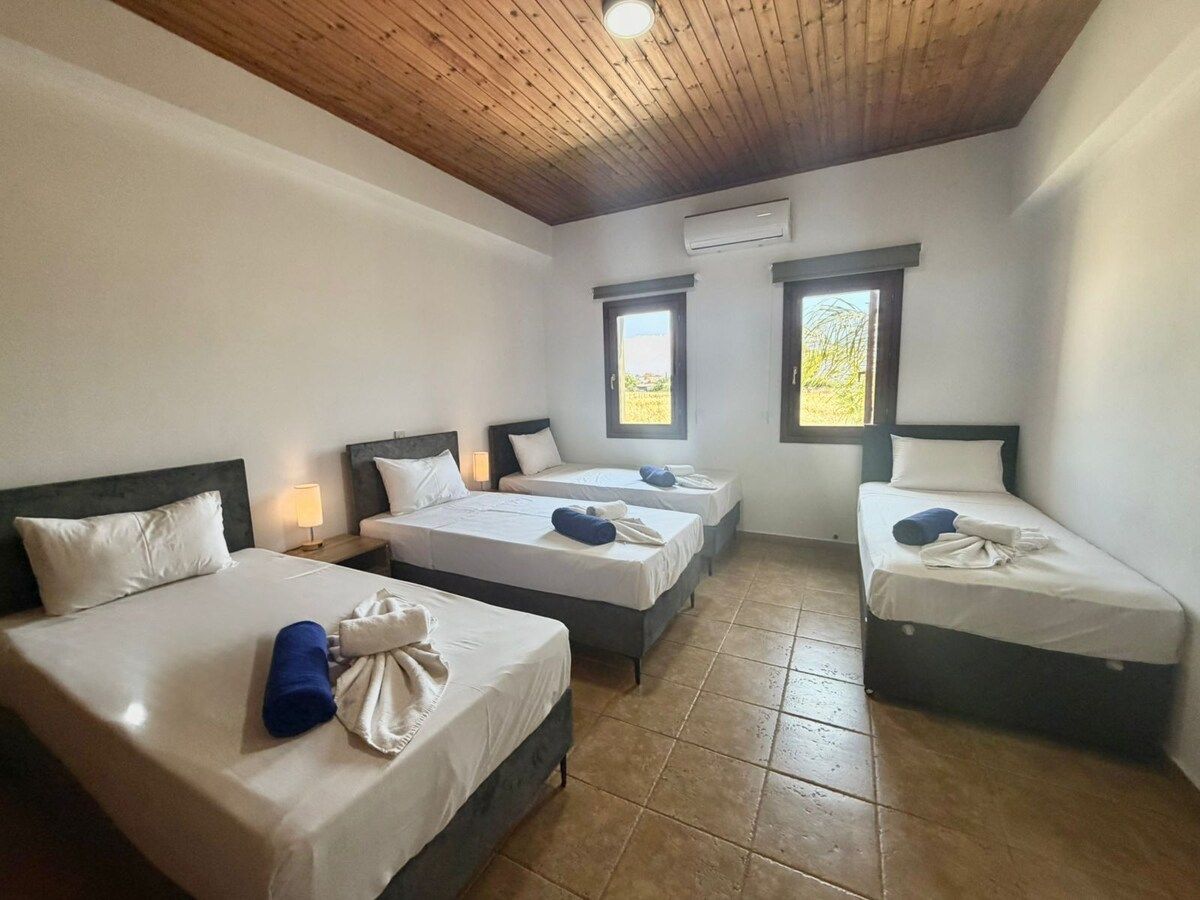 A hotel room with three beds, a wooden ceiling, and a window.