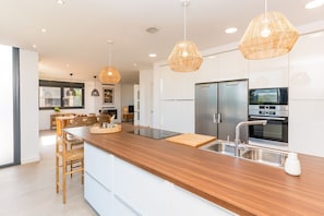 Eine moderne Küche mit einer Holz Arbeitsplatte, Edelstahlgeräten und Korbtropfleuchten.