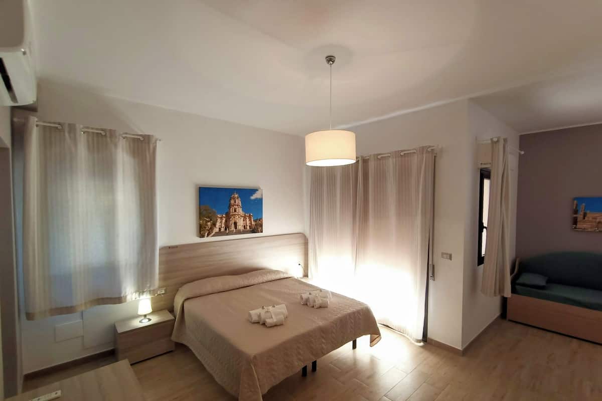A hotel room with a bed, a nightstand, a lamp, a painting, and a sofa.