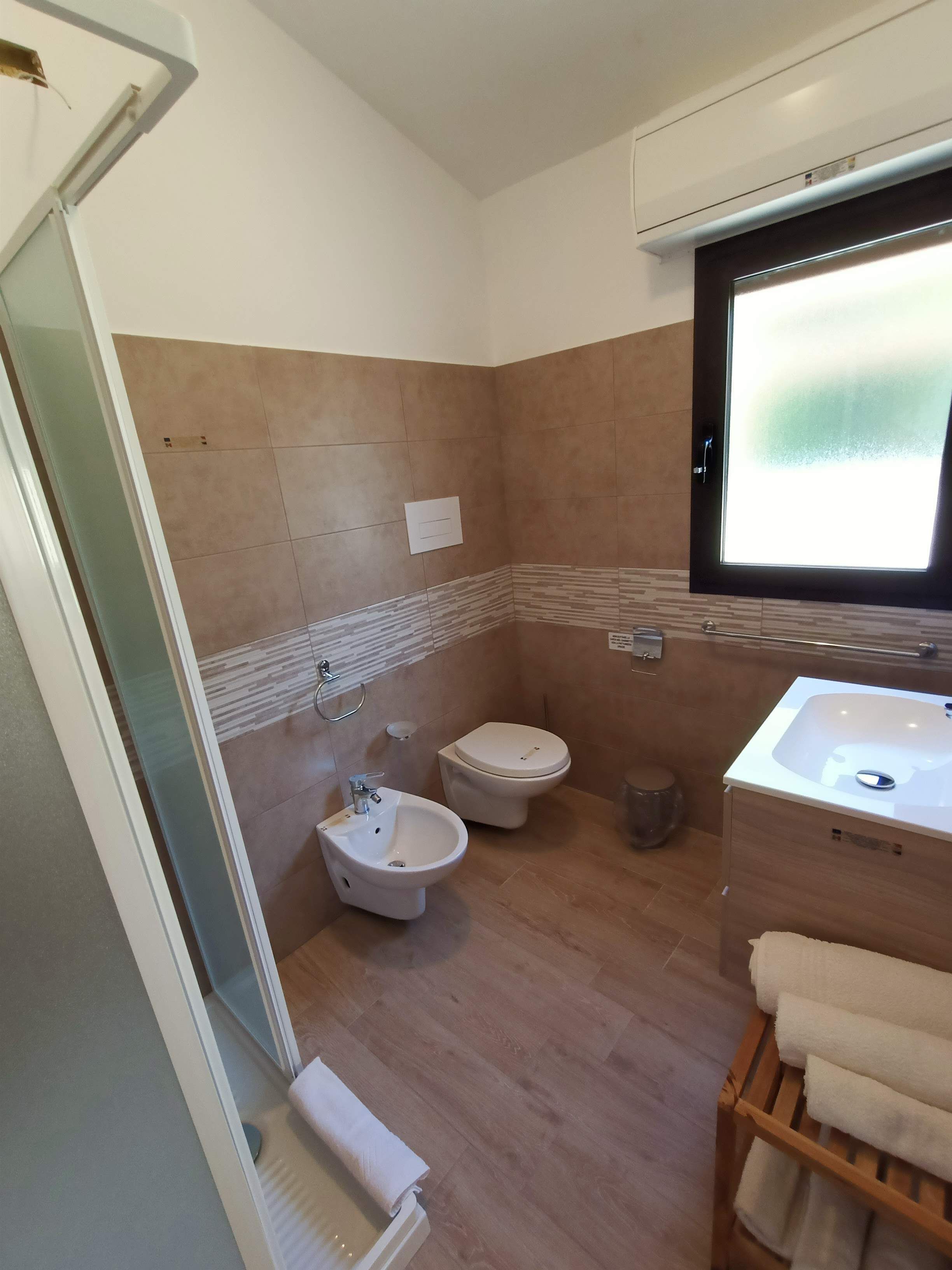 Een badkamer met een bidet, toilet, wastafel en een raam met geëtste glas.