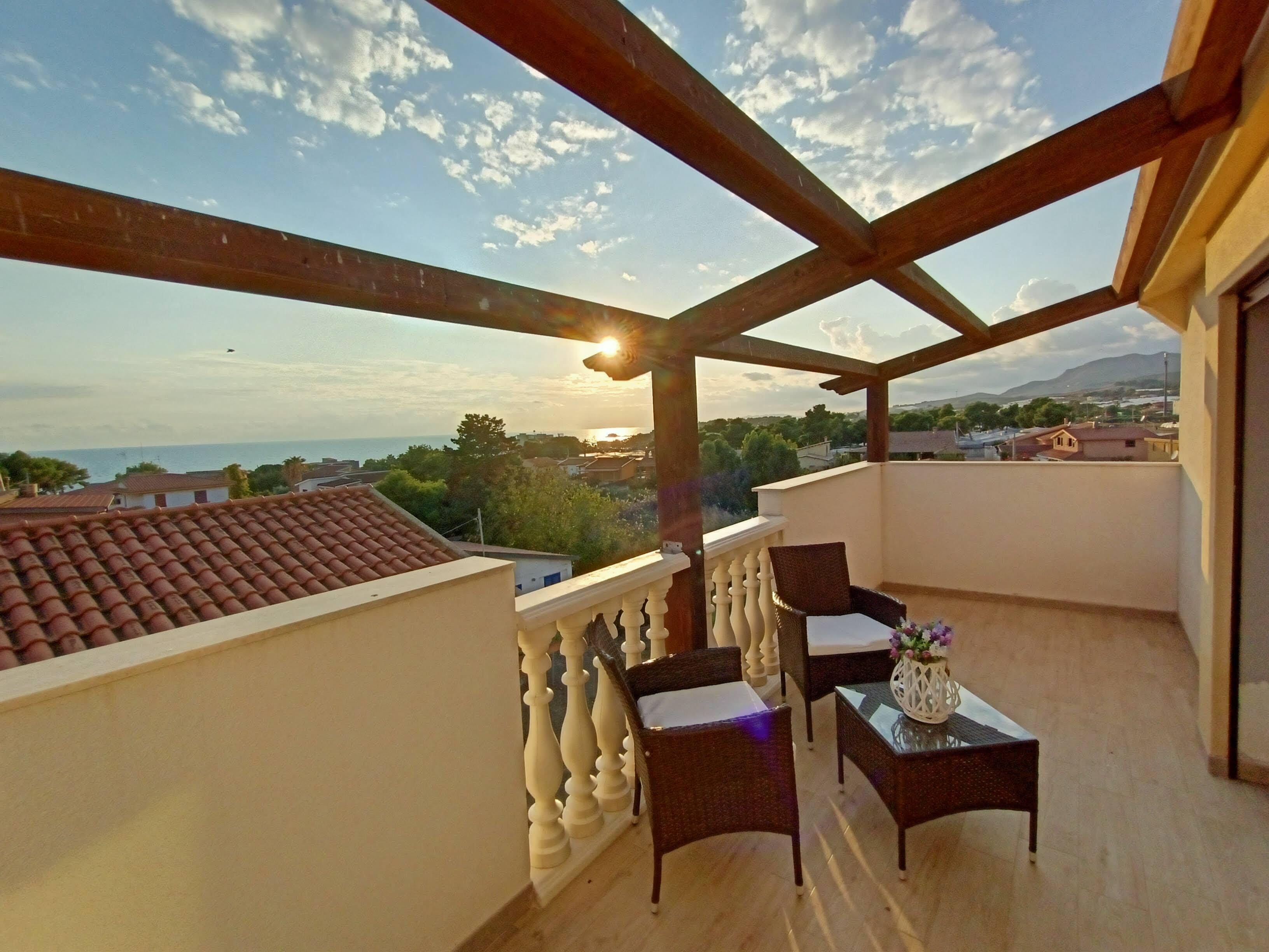 A balcony with a view of the sea, wooden pergola, and two wicker chairs.