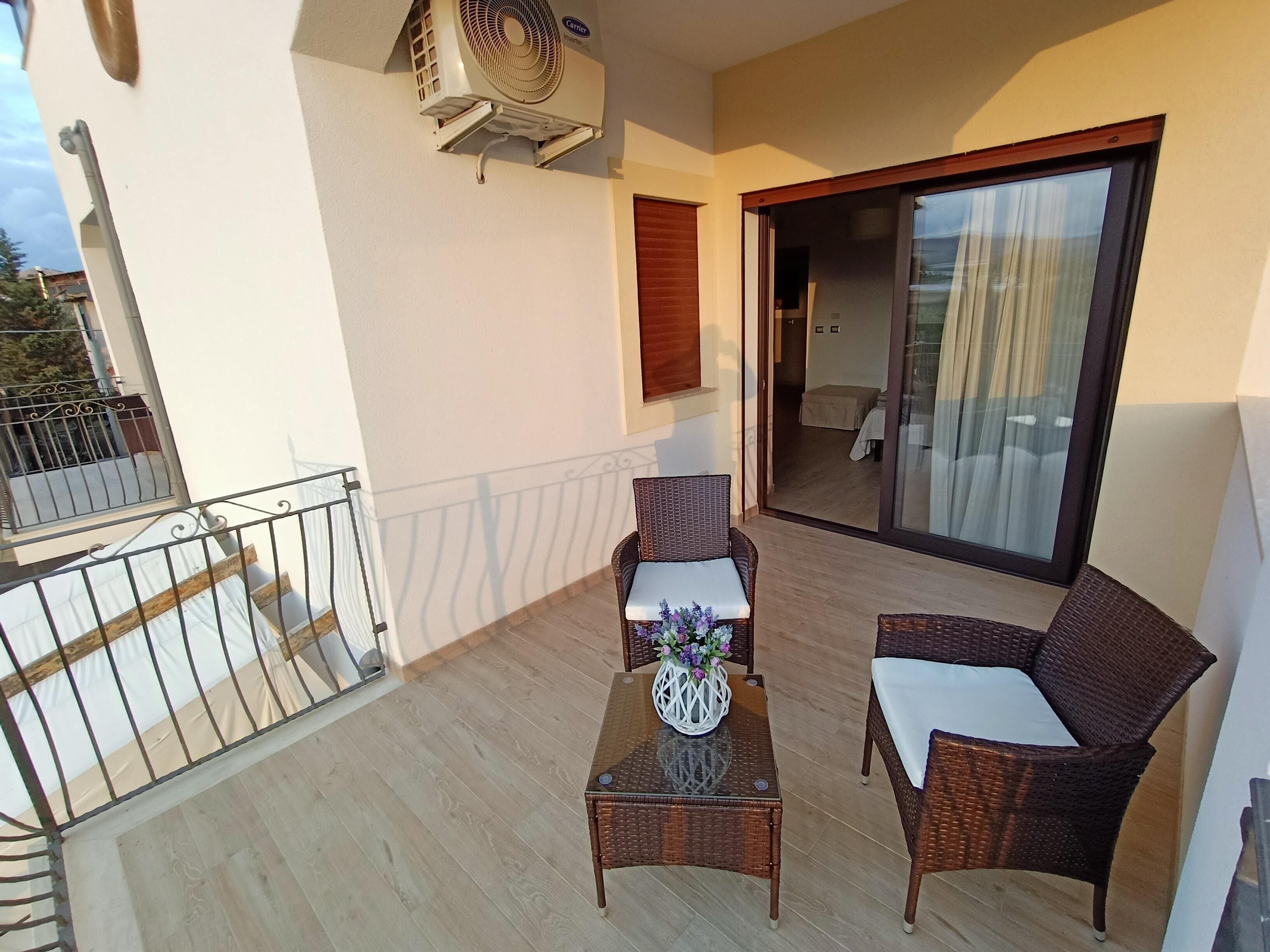 A balcony with wicker furniture, a glass table, and a potted plant.