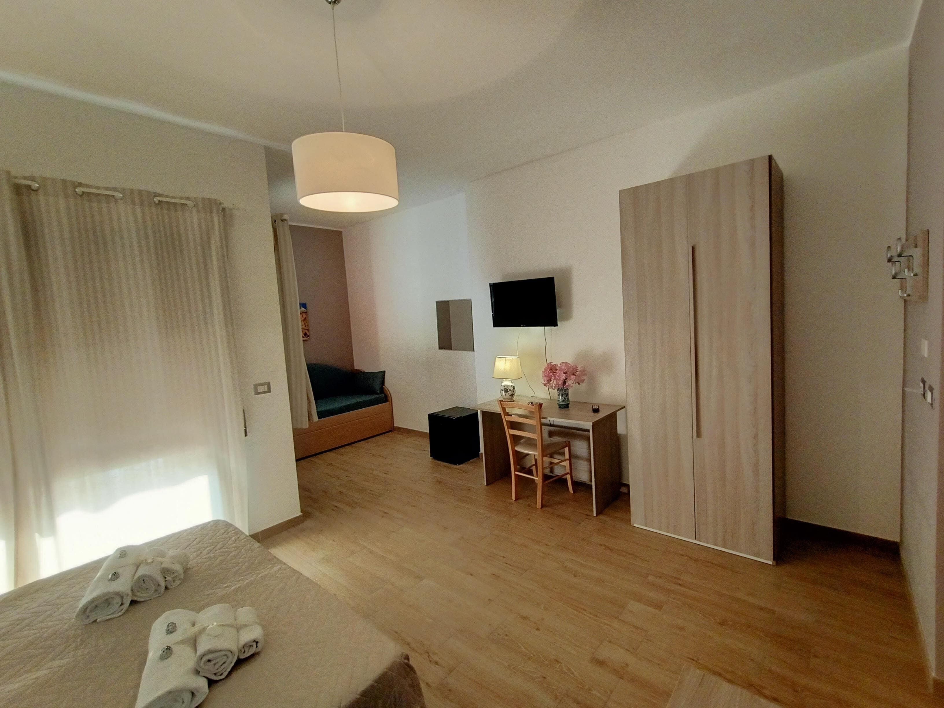 A hotel room with a bed, a desk with a chair, a television, and a wardrobe.