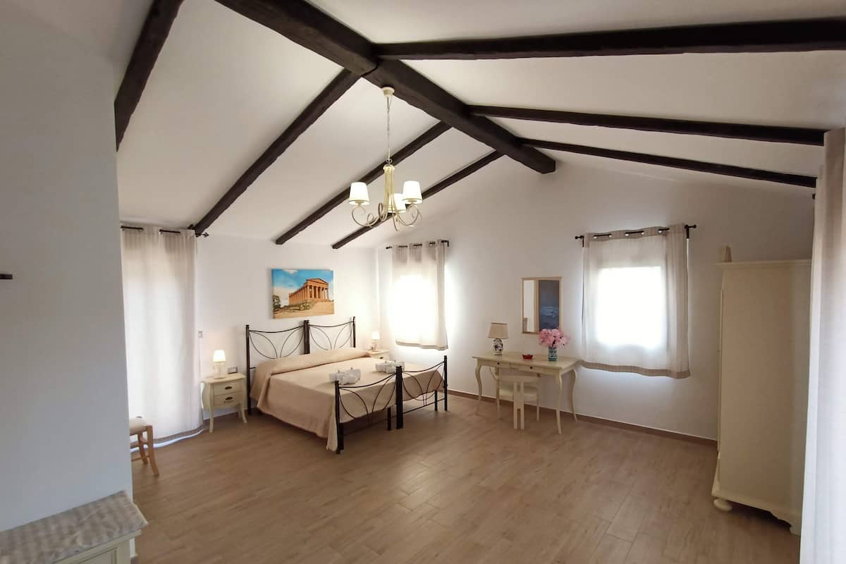 A bedroom with a bed, bedside tables, a desk, a chair, a mirror, and a painting on the wall.