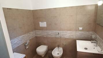 Un baño con inodoro, bidé y lavamanos, suelo de madera y un perchero para toallas.