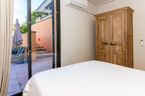 A bedroom with a bed, a wooden wardrobe, and a sliding glass door leading to an outdoor area with steps and a patio umbrella. - Villa Dumas I - Five Bedroom Villa, Sleeps 12 (Sitges)