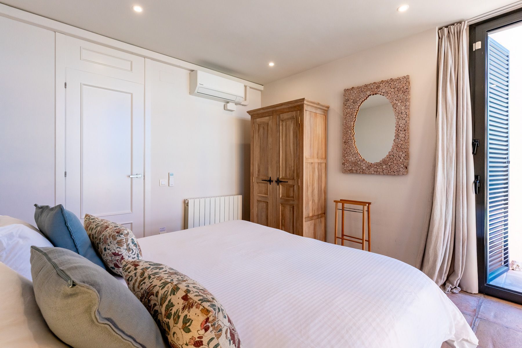 A bedroom with a bed, a wardrobe, a radiator, a mirror, and a window with curtains.