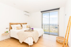 Ein Schlafzimmer mit einem Bett, einem Nachttisch, einer kleinen Pflanze, einem Tablett mit einer Karaffe und Blumen sowie einem Balkon mit Blick.