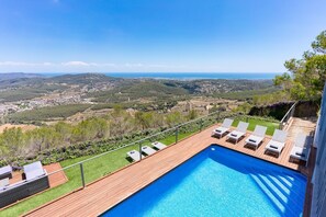 Ein Pool mit Liegestühlen, einer Holzterrasse und Blick auf die Landschaft.