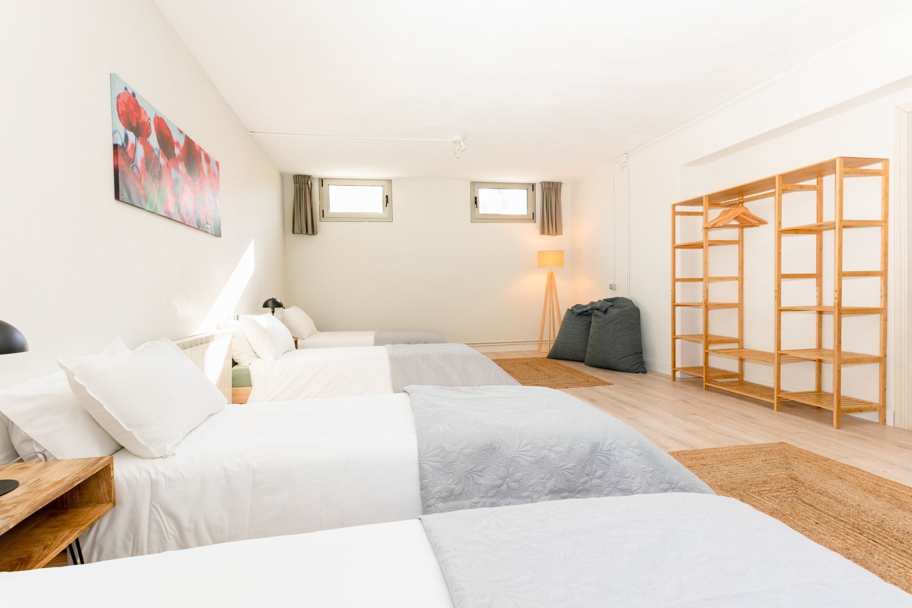 A hotel room with two beds, a wooden wardrobe, a lamp, and a painting on the wall.