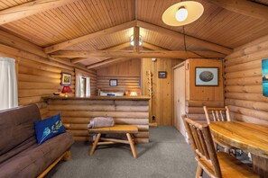 Interior de una cabaña de troncos con un banco de madera, una mesa de madera y un sofá con cojín.