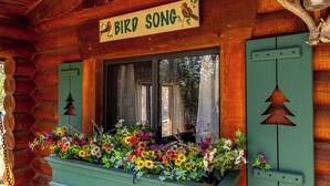 A wooden cabin with a window displaying colorful flowers and a sign reading 'BIRD SONG'. - New! Birdsong Log Cabin, Mountain views, firepit (Bigfork)