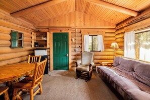 A log cabin interior with a dining table, chairs, a sofa, a green door, and a window with curtains. - New! Bears Den Log Cabin, Mountain views, firepit (Bigfork)