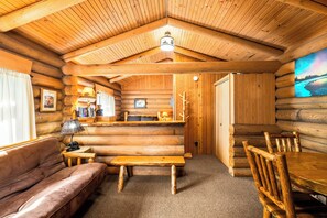 L’intérieur d’une cabane en rondins, avec un canapé, un banc en bois, une table à manger et des chaises.