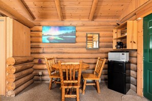 A log cabin interior with a wooden dining table, chairs, a refrigerator, and a painting on the wall. - New! Bears Den Log Cabin, Mountain views, firepit (Bigfork)