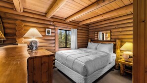 Quarto de cabana de madeira com uma cama, abajures, uma janela com cortinas e teto de madeira.