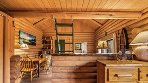 Interior de uma cabana de tronco com área de jantar, móveis de madeira, uma escada e um quadro na parede.